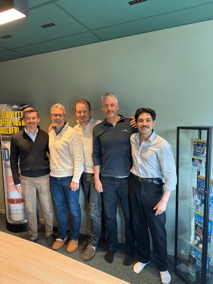 The GilTor and Done teams together at the office, with a Finish display in the background.